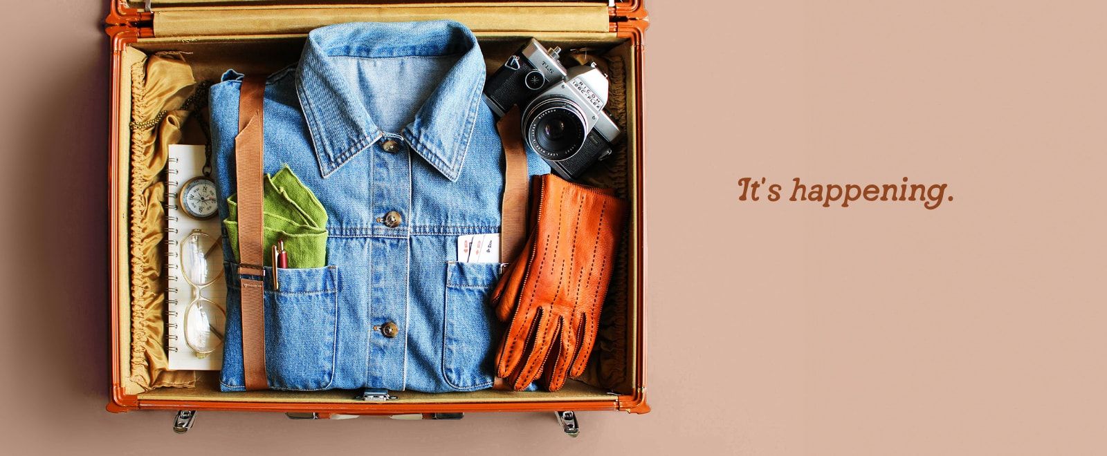 A vintage suitcase filled with clothes, a notebook, a camera and gloves.