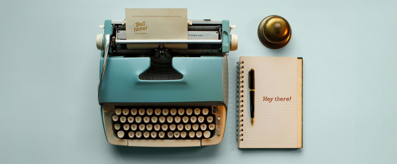 A blue typewriter with Bell Hotel stationary next to a notebook and bell.